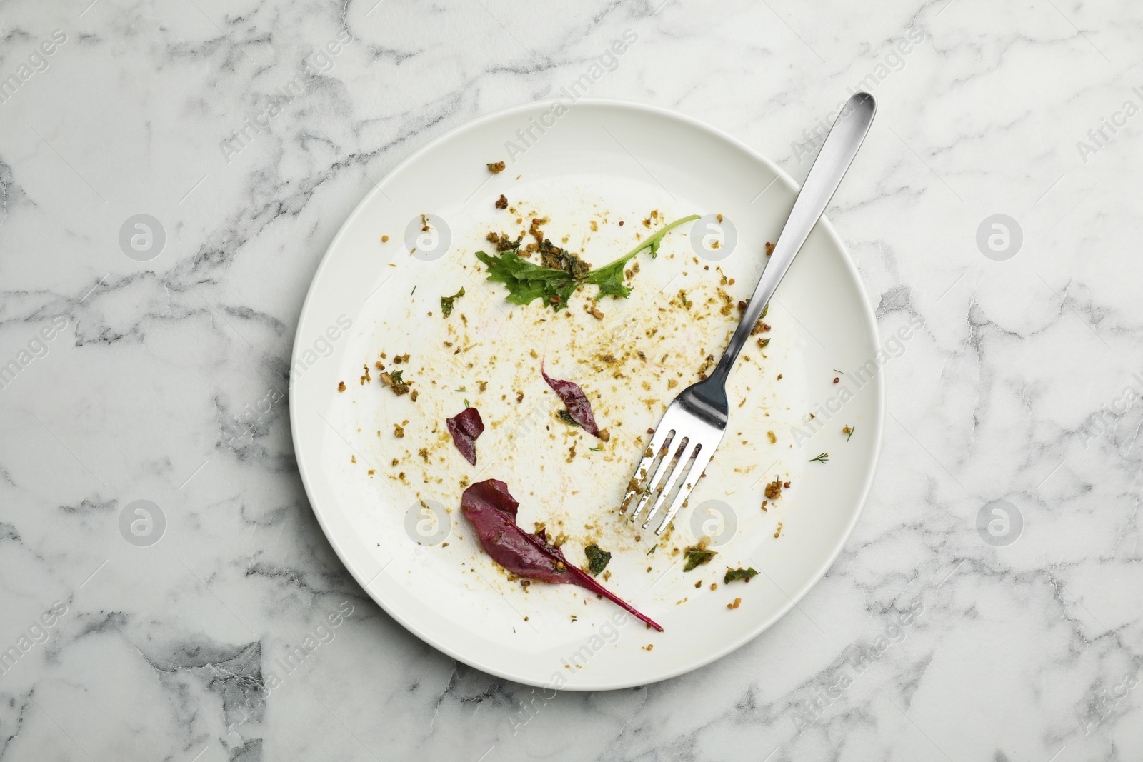 Photo of Dirty plate with food leftovers, herbs and fork on marble background, top view