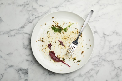 Photo of Dirty plate with food leftovers, herbs and fork on marble background, top view