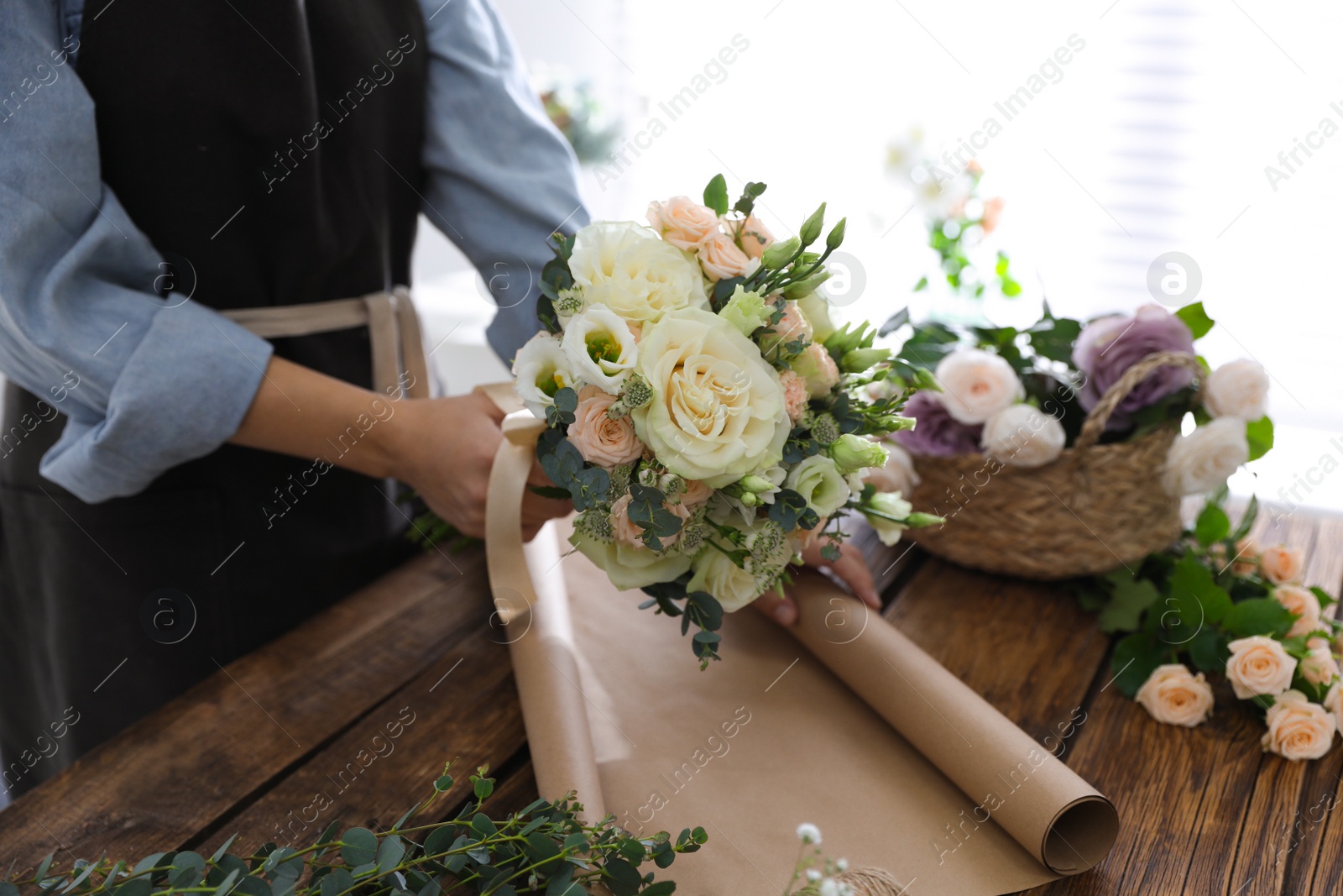 Photo of Florist making beautiful wedding bouquet at wooden table, closeup