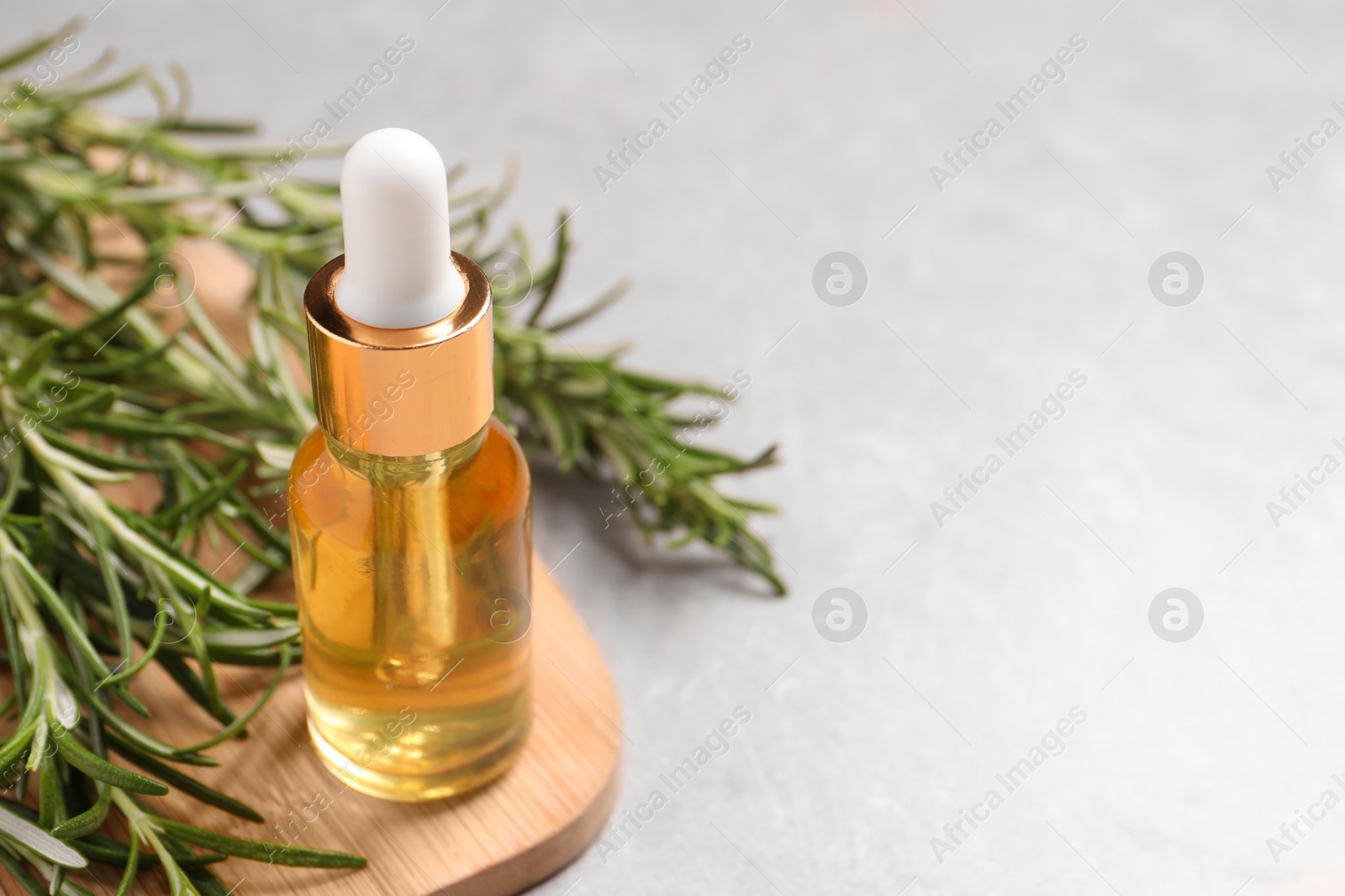 Photo of Bottle of essential oil and fresh rosemary on light grey table, closeup. Space for text