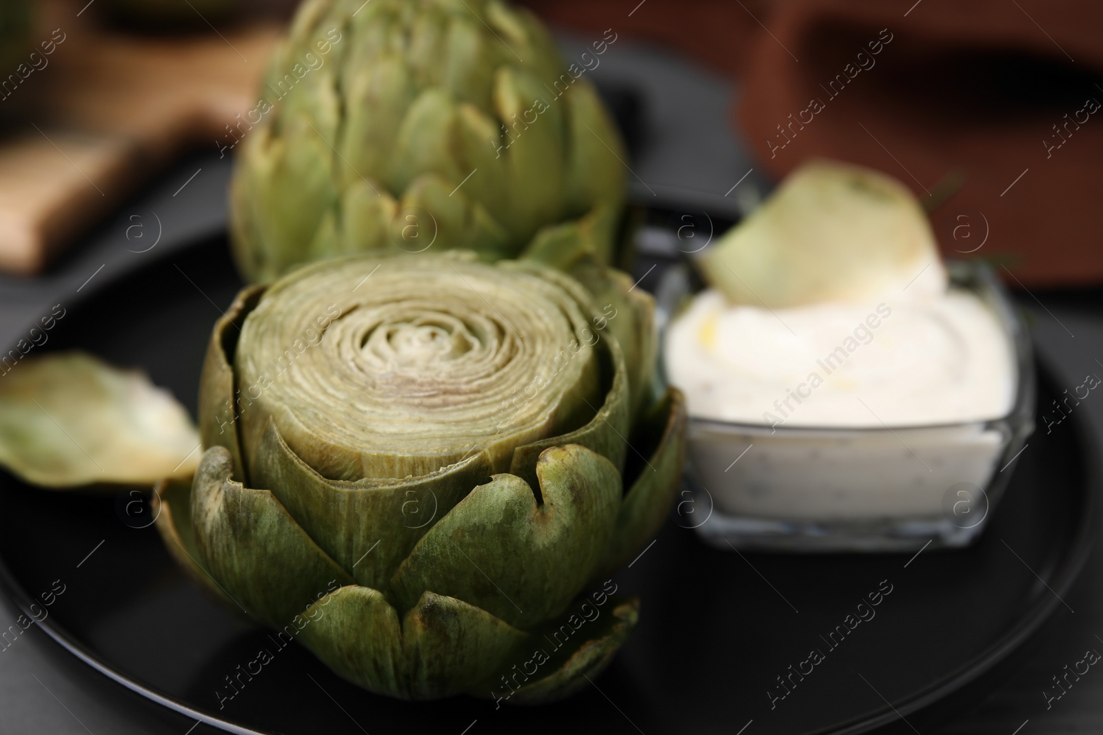 Photo of Delicious cooked artichokes with tasty sauce on plate, closeup