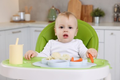 Cute little baby with healthy food in high chair at home