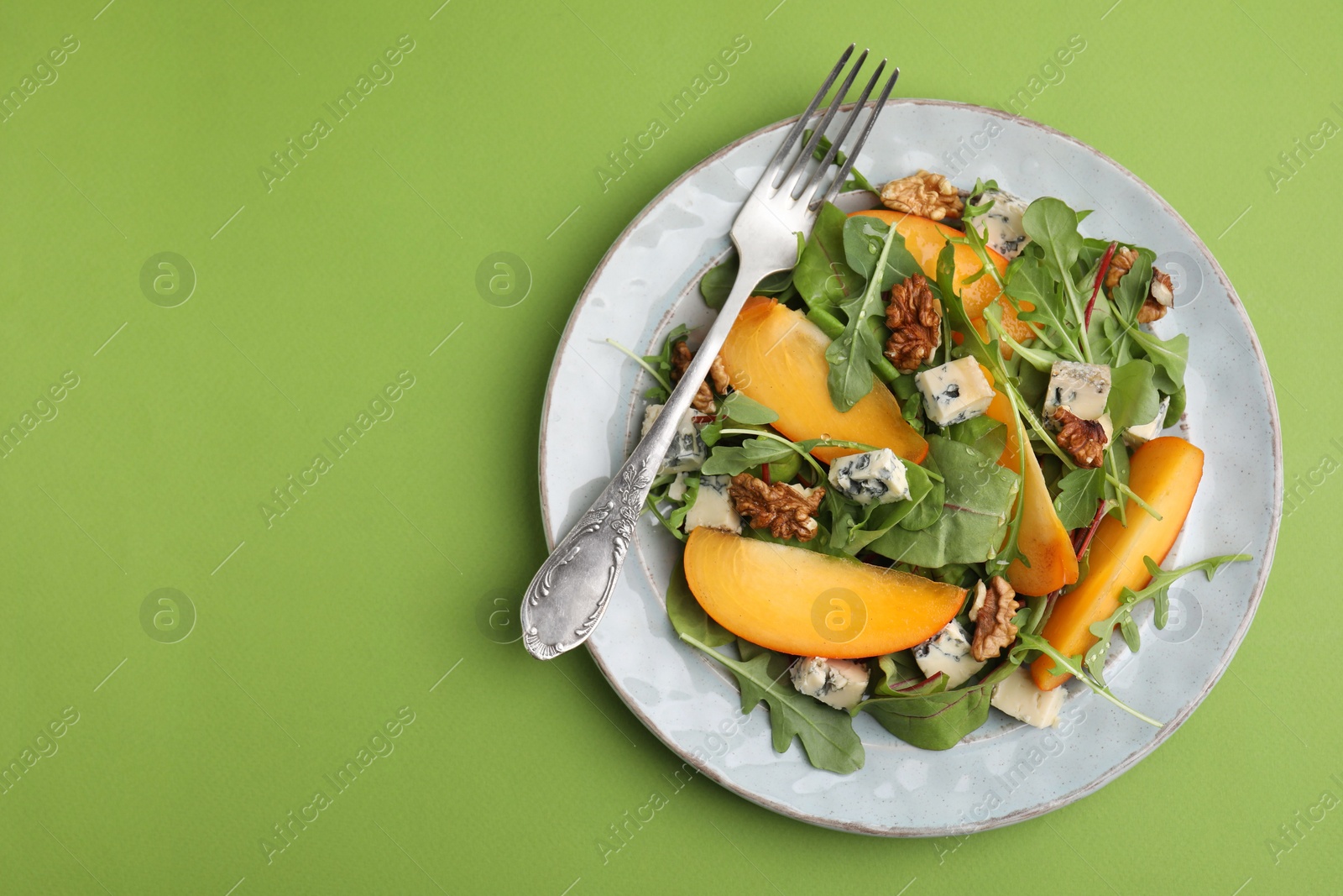 Photo of Tasty salad with persimmon, blue cheese and walnuts served on light green background, top view. Space for text