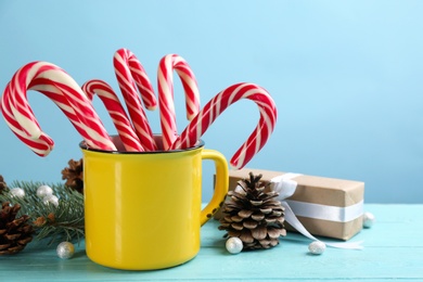 Photo of Many sweet candy canes in cup, gift box and Christmas decor on light blue wooden table. Space for text