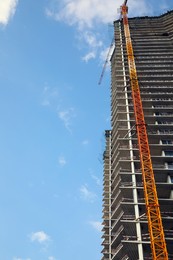 Photo of Construction site with tower crane near unfinished building under cloudy sky, low angle view