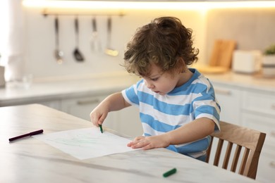 Photo of Cute little boy drawing with marker at table in kitchen