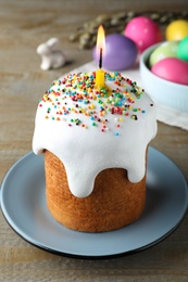 Photo of Easter cake with burning candle on wooden table