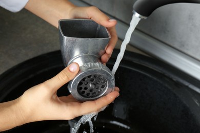 Photo of Woman washing manual meat grinder under tap water in kitchen sink indoors, closeup
