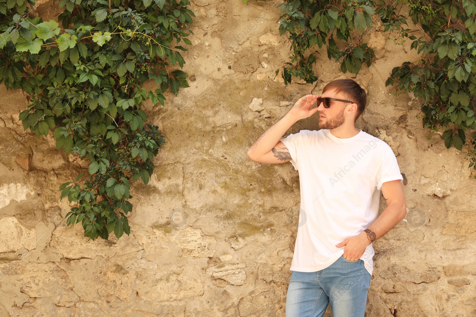 Photo of Young man wearing white t-shirt near stone wall on street