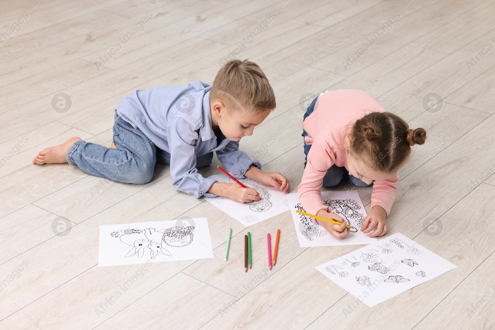 Photo of Cute little children coloring drawings on warm floor indoors. Heating system