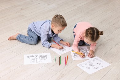 Photo of Cute little children coloring drawings on warm floor indoors. Heating system
