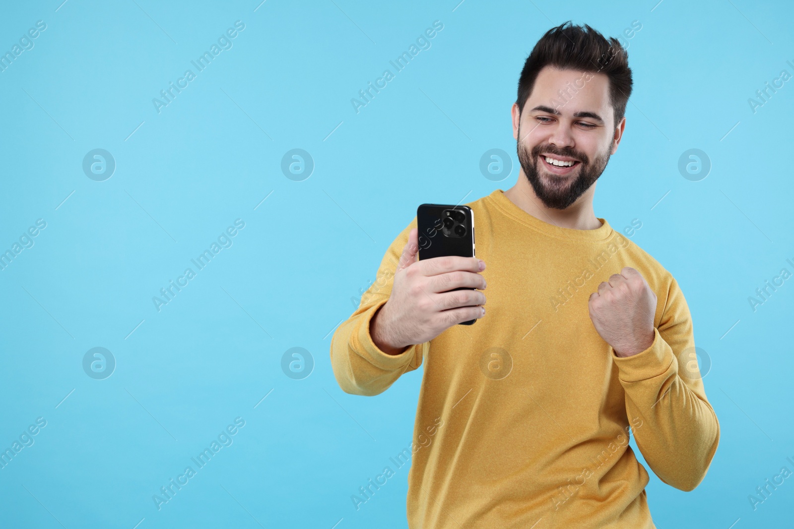 Photo of Happy young man using smartphone on light blue background, space for text