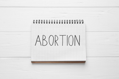 Photo of Notebook with word Abortion on white wooden background, top view