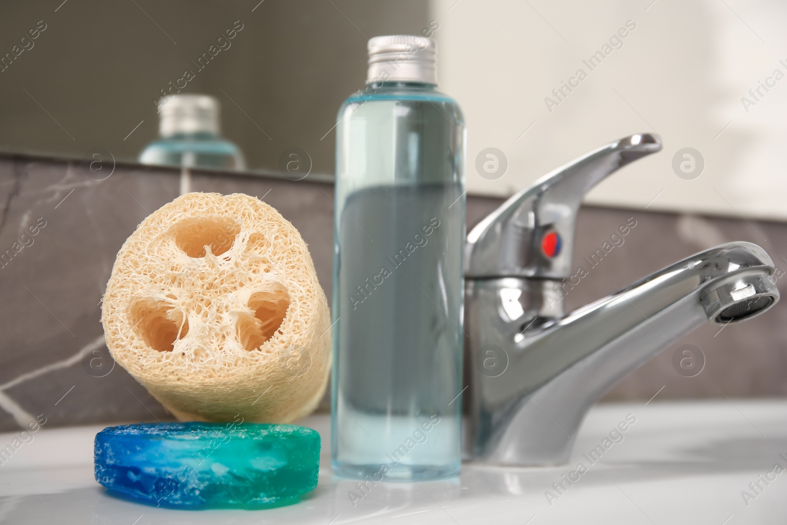 Photo of Loofah sponge and cosmetic products on sink in bathroom, closeup