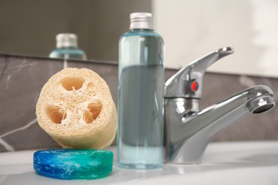 Photo of Loofah sponge and cosmetic products on sink in bathroom, closeup