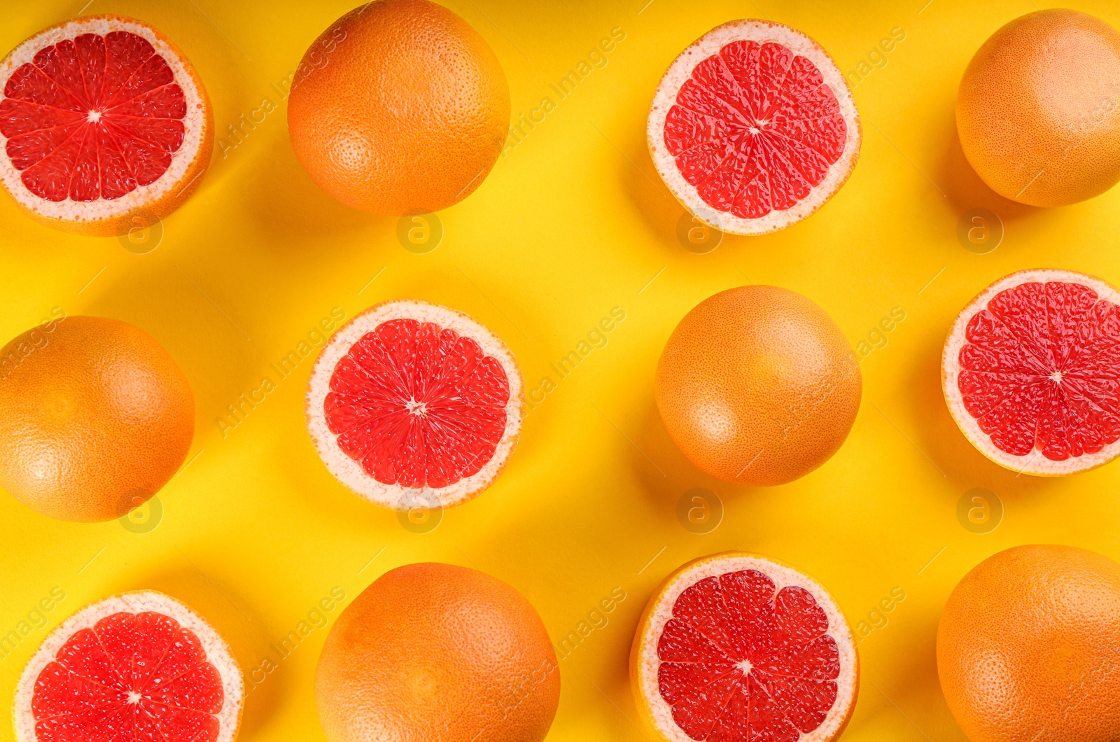 Photo of Cut and whole ripe grapefruits on yellow background, flat lay