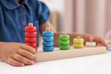 Photo of Motor skills development. Little girl playing with stacking and counting game at table indoors, closeup
