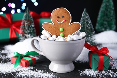 Photo of Gingerbread man in cup on black table against blurred lights