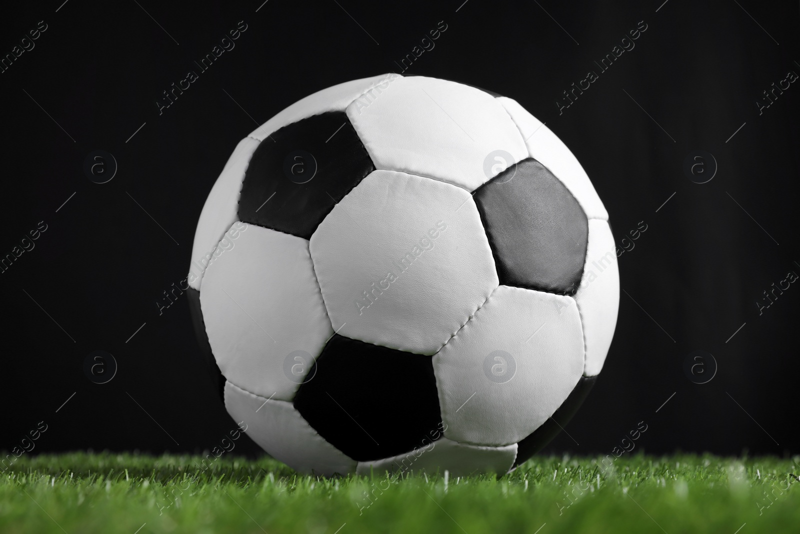 Photo of Football ball on green grass against black background