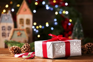 Photo of Christmas present. Beautiful gift box, cones and candy canes on wooden table against blurred festive lights, space for text