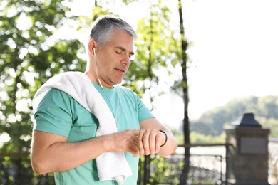 Photo of Handsome mature man looking at fitness tracker in park. Healthy lifestyle