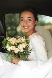 Photo of Young bride wearing wedding dress with beautiful bouquet in automobile