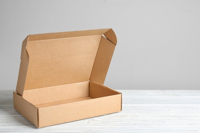 Photo of Open cardboard box on white wooden table against beige background, space for text