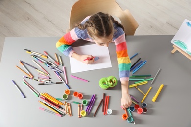 Photo of Little girl painting picture at table with painting tools indoors, top view