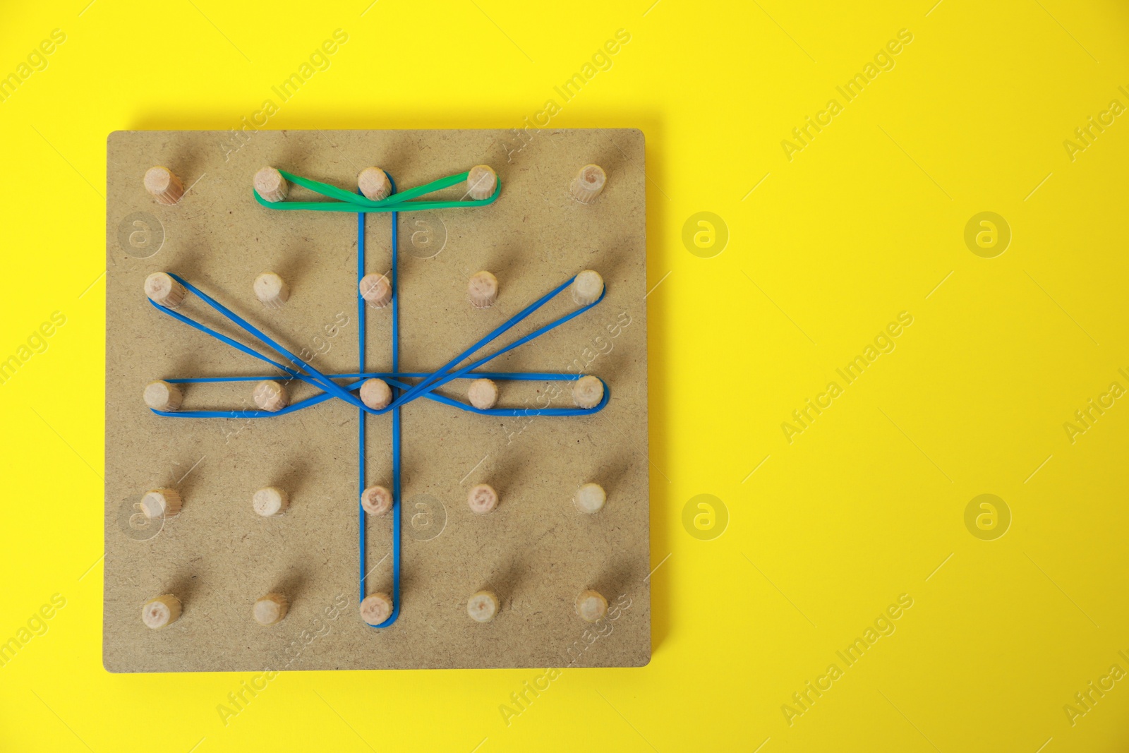 Photo of Wooden geoboard with dragonfly shape made of rubber bands on yellow background, top view and space for text. Educational toy for motor skills development