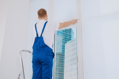 Photo of Worker installing roller window blind on stepladder indoors