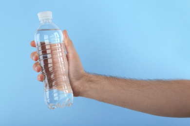 Man holding plastic bottle with water on color background