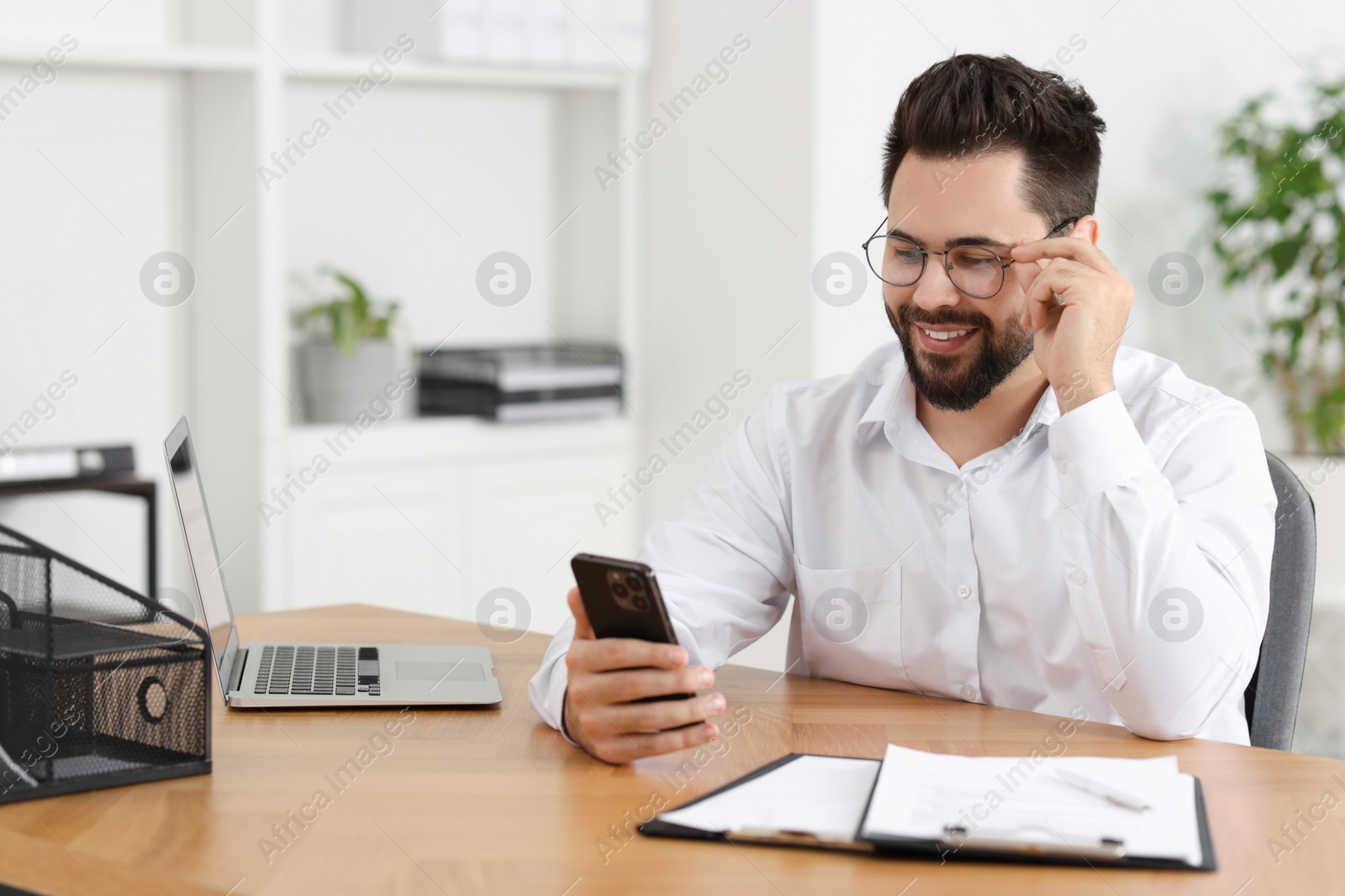 Photo of Handsome young man using smartphone at wooden table in office