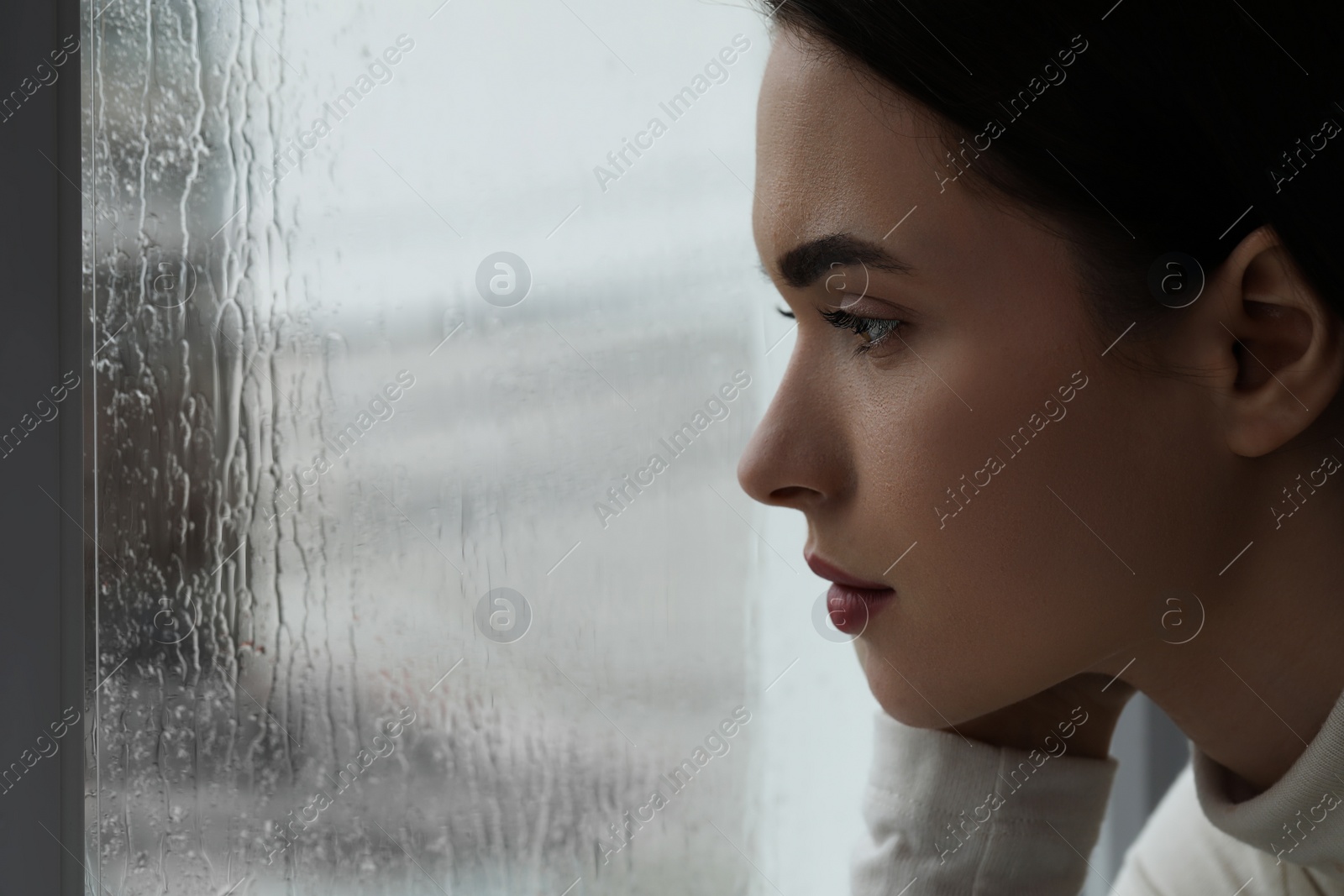 Photo of Melancholic young woman watching rain through window, closeup with space for text. Loneliness concept