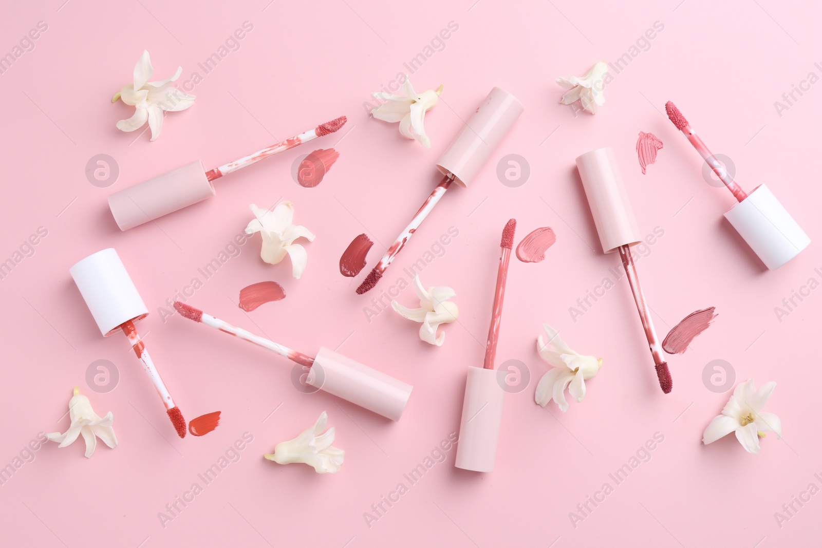 Photo of Different lip glosses, applicators and flowers on pink background, flat lay