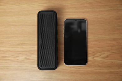 Photo of Portable bluetooth speaker and smartphone on wooden table, flat lay. Audio equipment