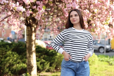 Beautiful woman near blossoming tree on spring day, space for text