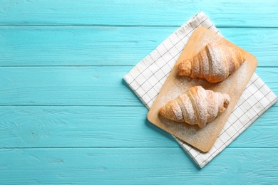 Wooden board with tasty croissants and space for text on light blue background, top view. French pastry