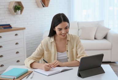 Photo of Young woman taking notes during online webinar at table indoors