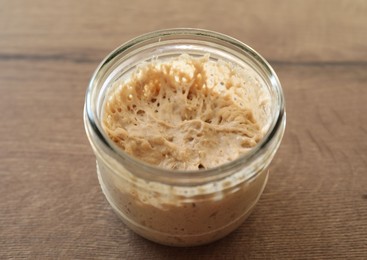Photo of Sourdough starter in glass jar on wooden table, closeup