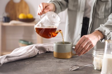 Photo of Woman pouring hot tea into cup at grey table, closeup