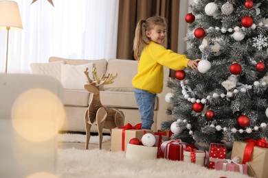Cute little girl decorating Christmas tree at home