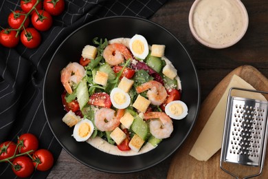 Photo of Delicious Caesar salad with shrimps and ingredients on wooden table, flat lay