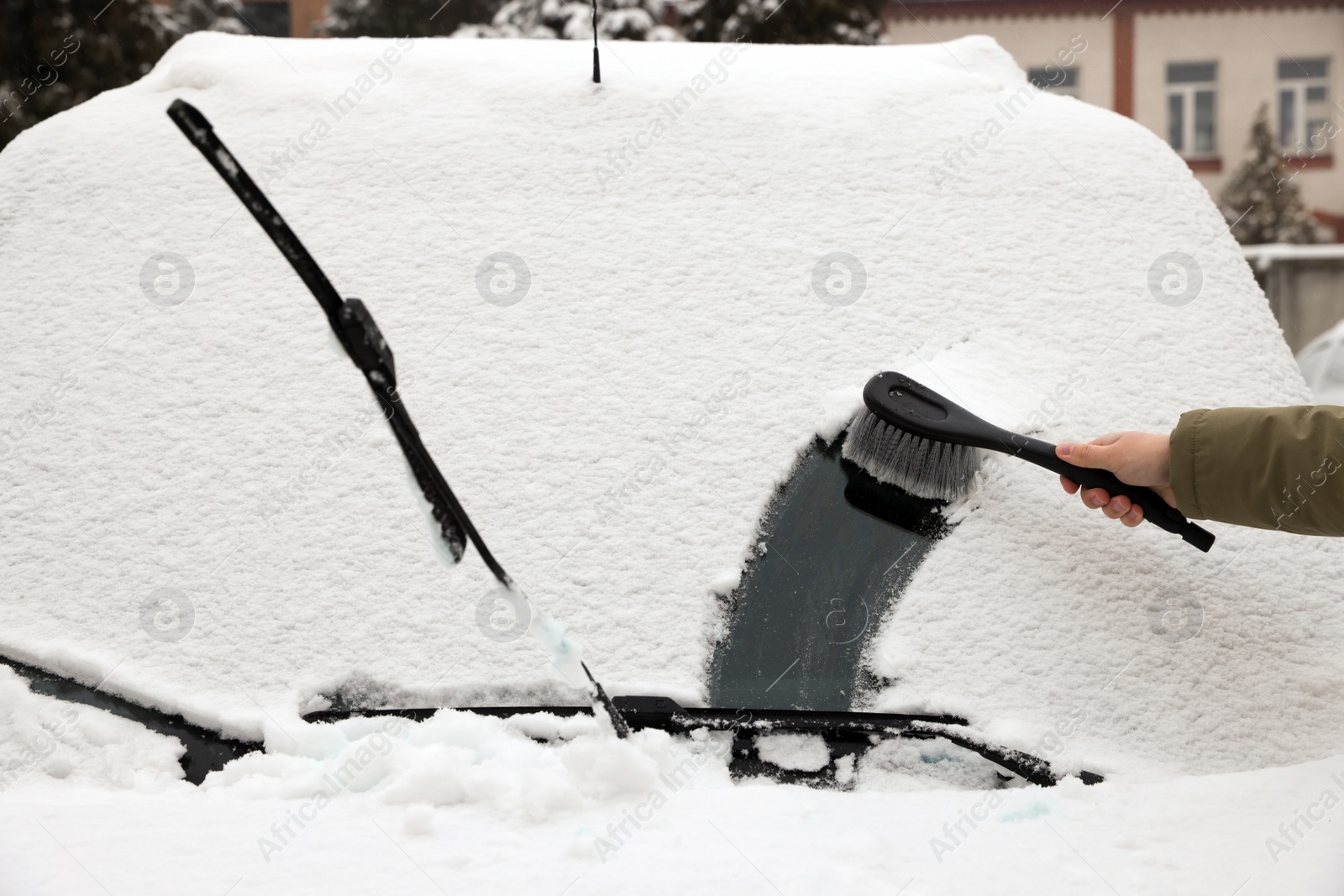 Photo of Woman cleaning car windshield from snow with brush outdoors, closeup