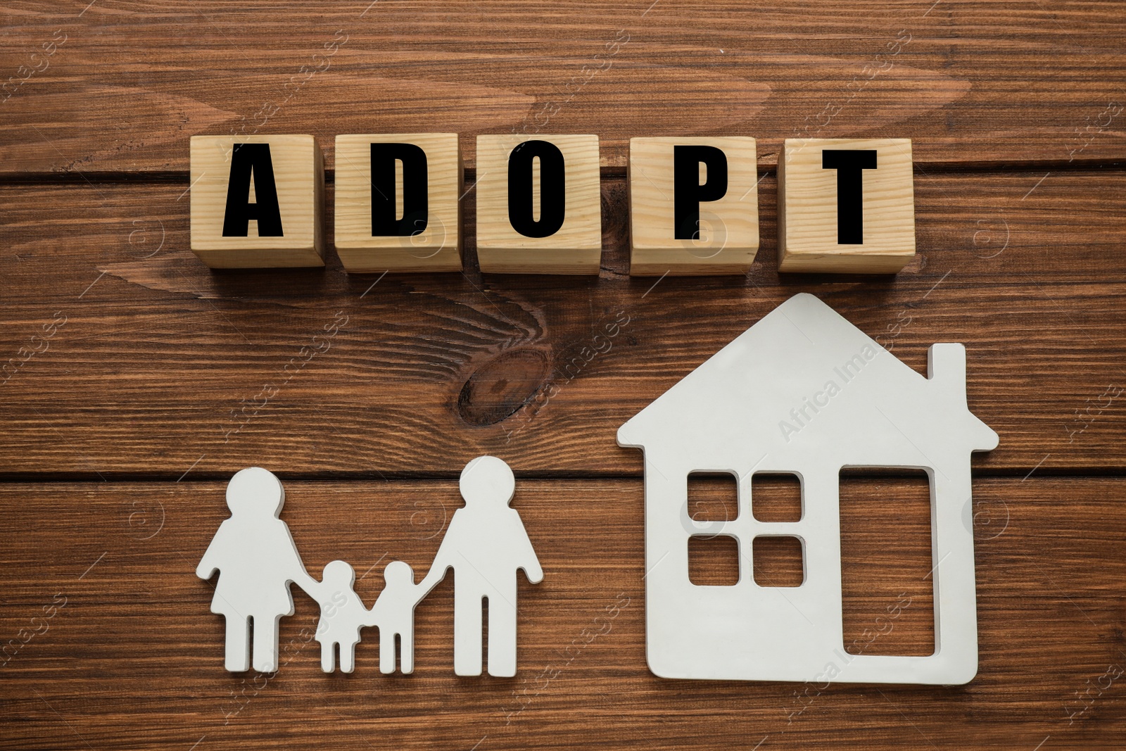 Photo of Family figure, house and word Adopt made of cubes on wooden table, flat lay