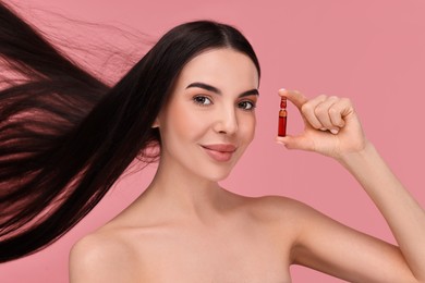 Photo of Beautiful young woman with long healthy hair holding ampoule on pink background