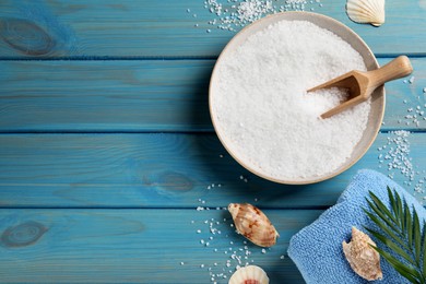 Photo of Bowl of natural sea salt, leaf and shells on light blue wooden table, flat lay. Space for text