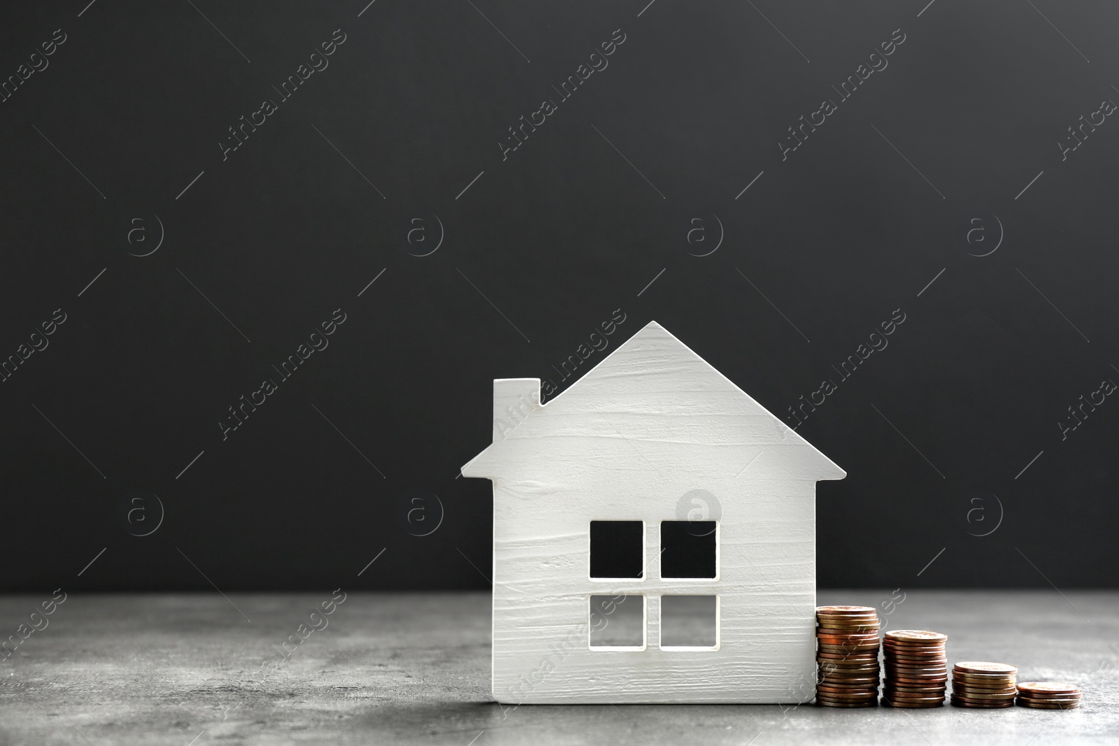 Photo of House figure and coins on table against dark background. Space for text