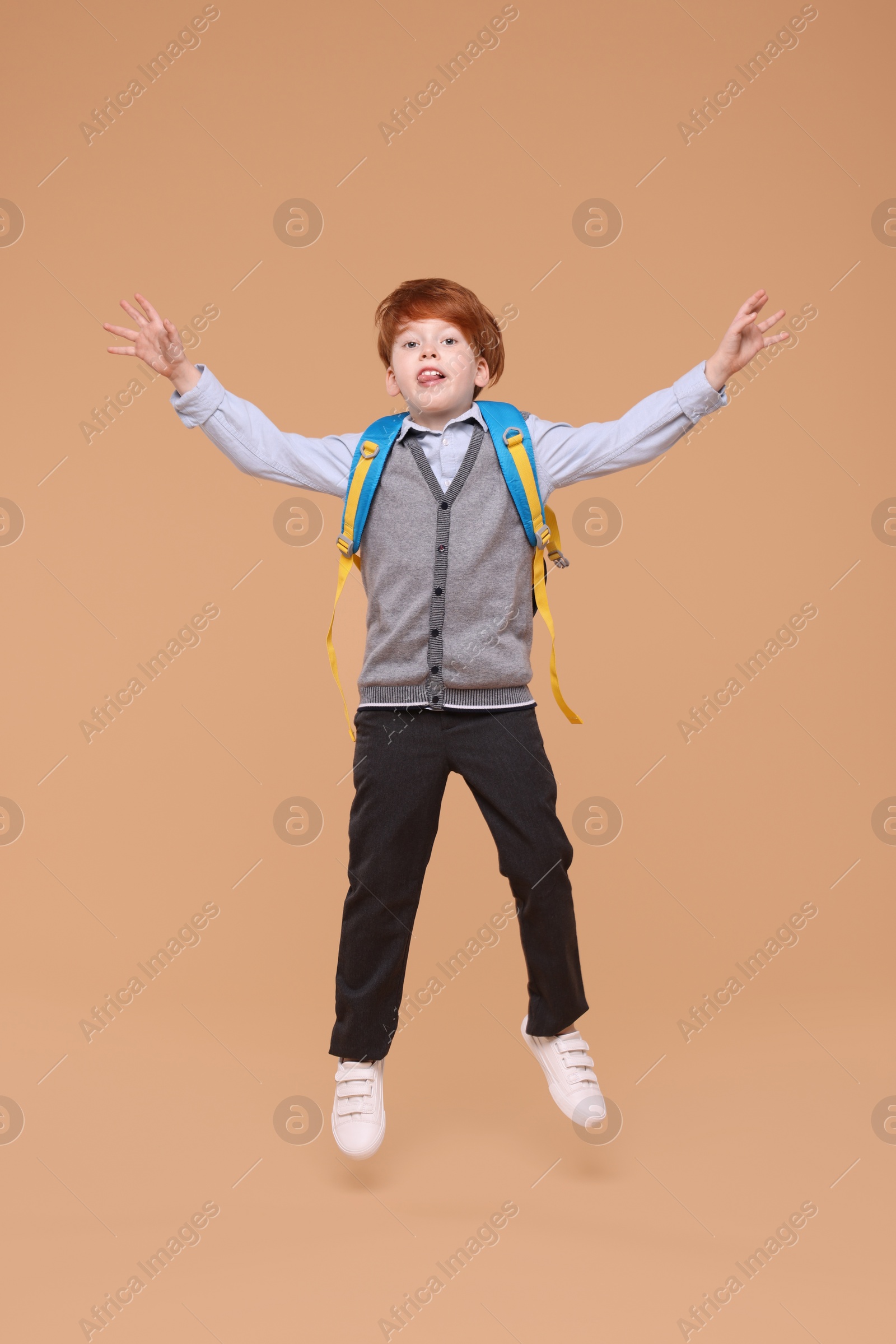 Photo of Funny schoolboy with backpack jumping on beige background