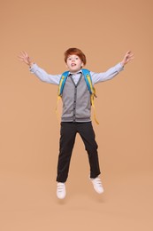 Photo of Funny schoolboy with backpack jumping on beige background