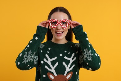 Happy young woman in Christmas sweater and funny glasses on orange background